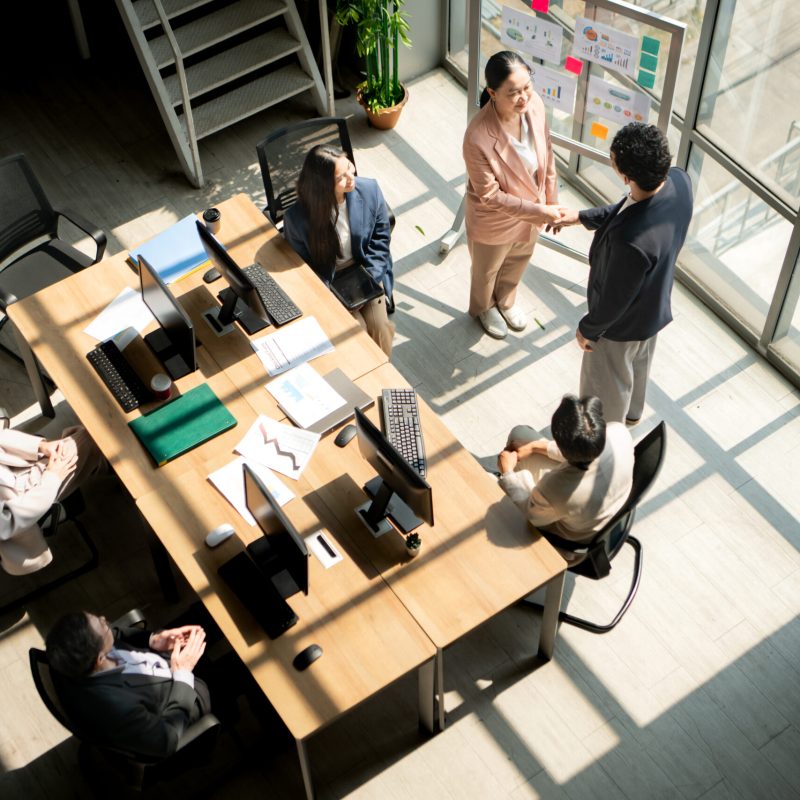 Top view of business colleagues shaking hands during a meeting near a presentation board, symbolizing agreement, cooperation, trust, and professional partnership